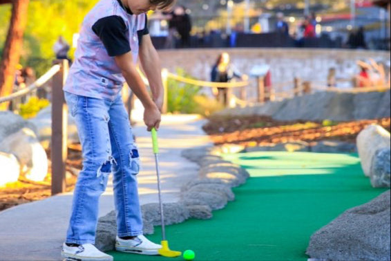 Child playing mini golf on a green course with a blurred background